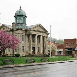 Red brick county courthouse with tall windows and a square clock tower behind a bare spring lawn under a flat gray sky